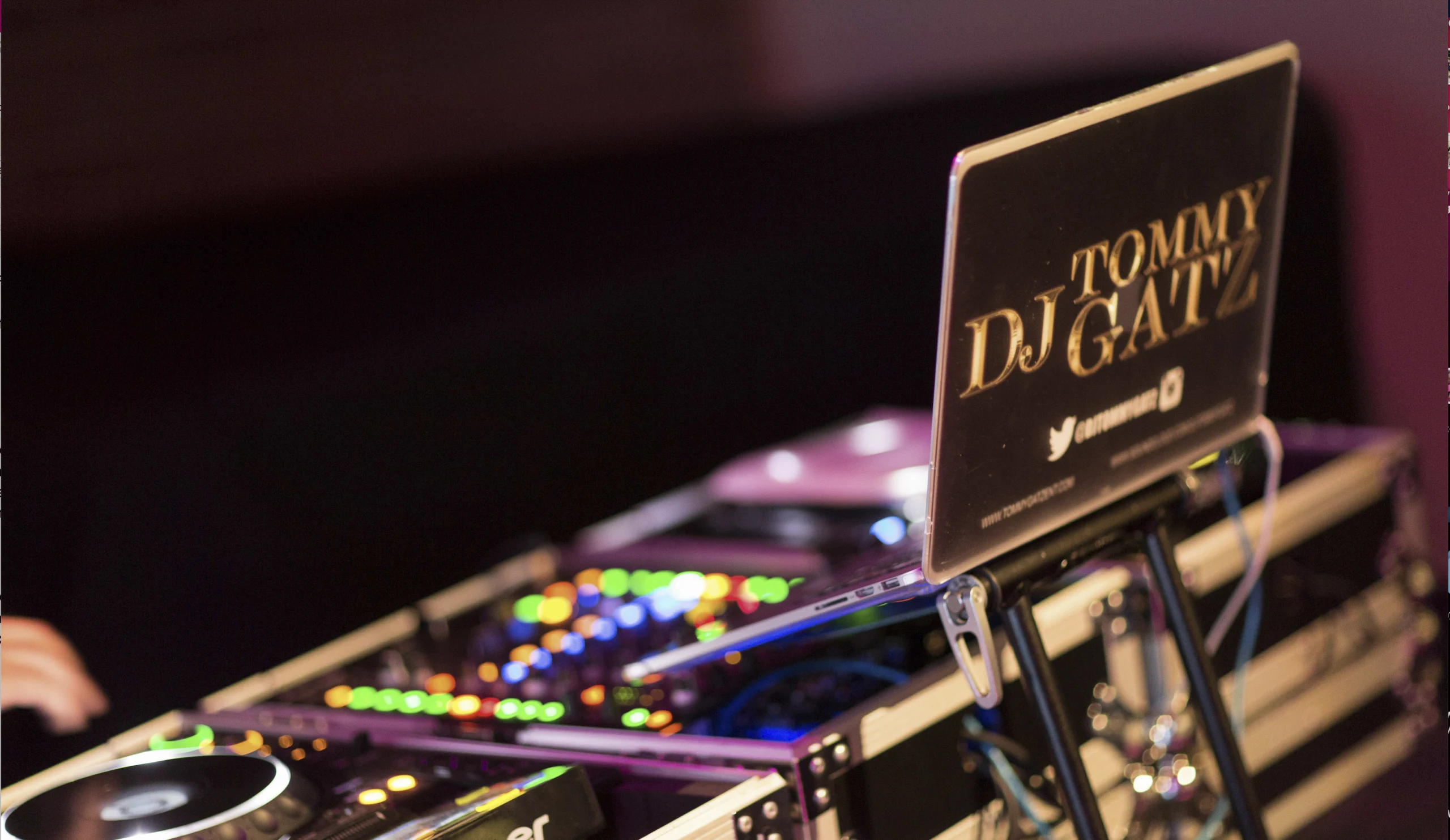 DJ equipment with illuminated buttons and a laptop displaying the name "DJ Tommy Gatz" and social media handles.