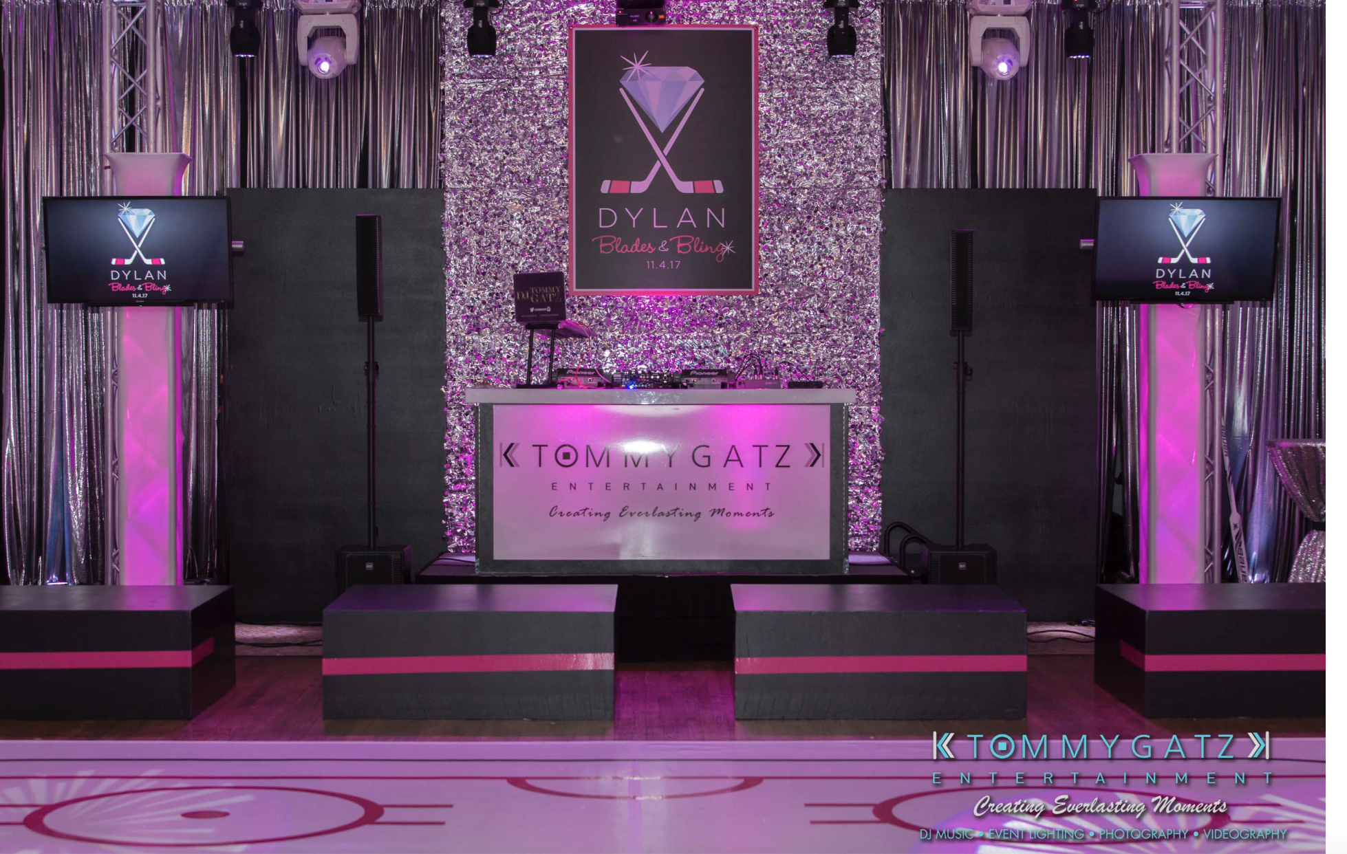 DJ booth setup at an event with pink and purple lighting. Two screens display the name "Dylan," and "Tommy Gatz Entertainment" branding is visible on the booth.