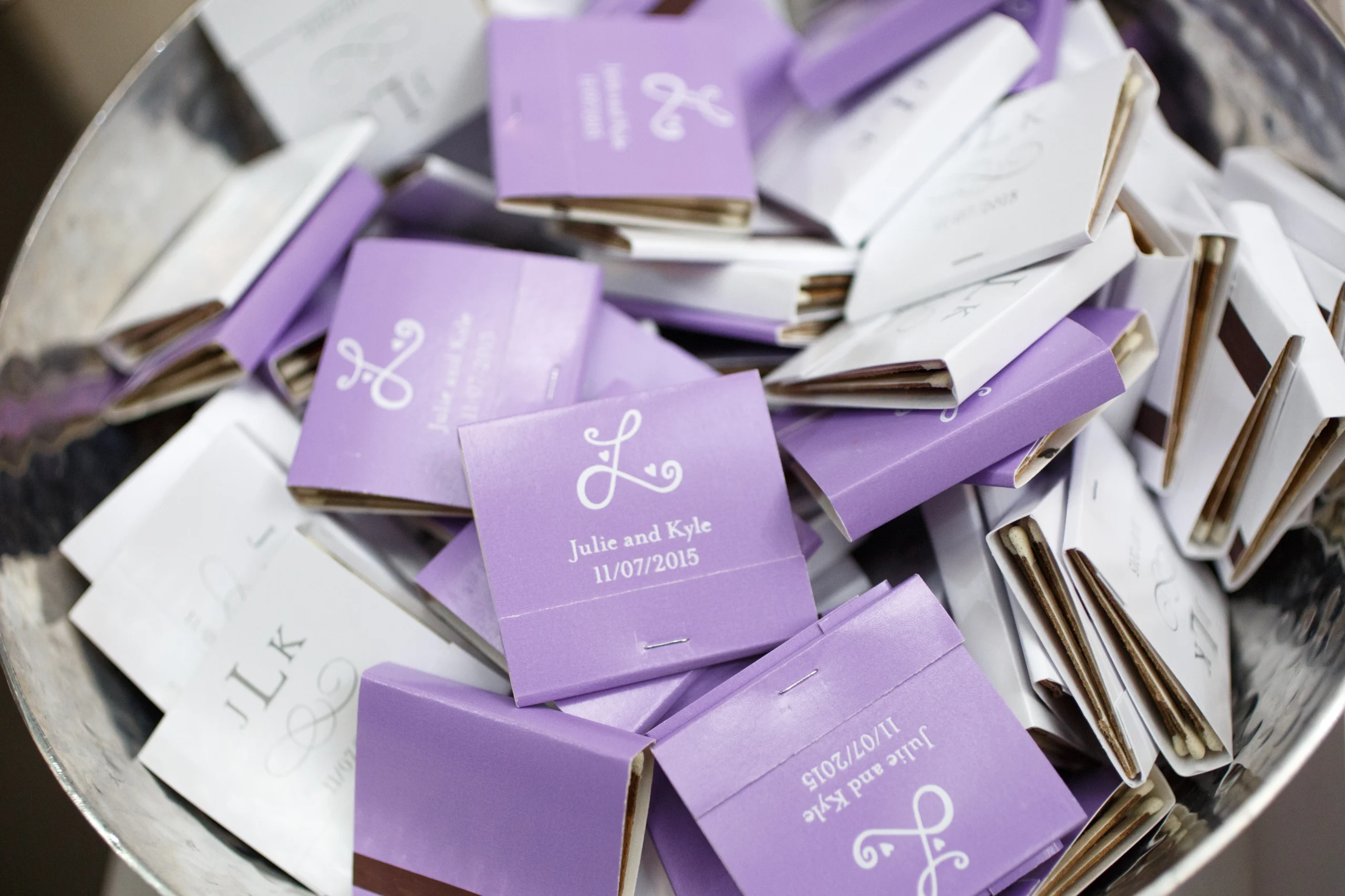 A bowl filled with purple and white matchbooks customized with "Julie and Kyle 11/07/2015" printed on the covers.