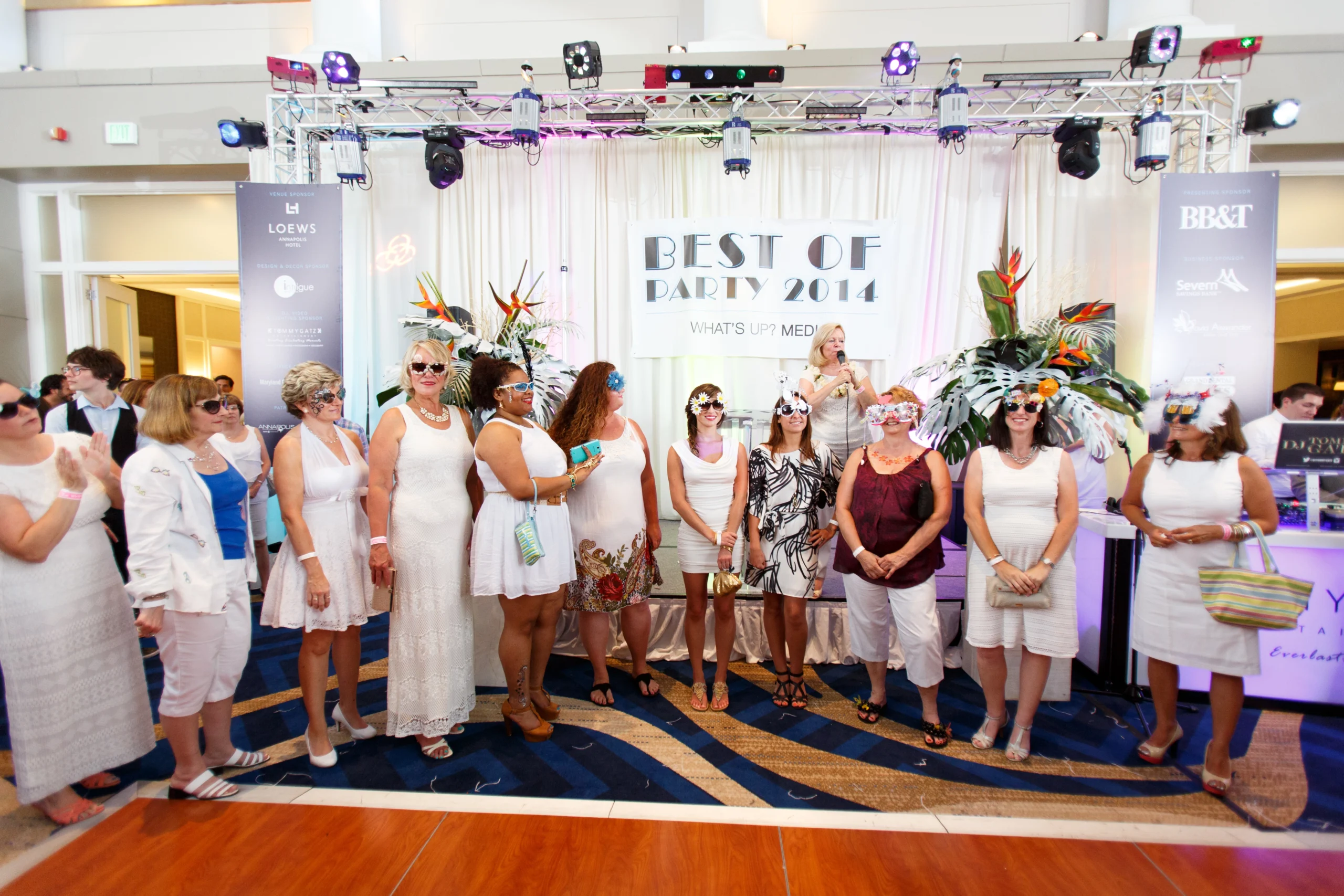 A group of people in white attire stand together at an indoor event with a "Best of Party 2014" backdrop.